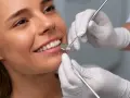 Uśmiechnięta kobieta podczas badania stomatologicznego. Dentysta sprawdza zęby, by upewnić się, że bonding nie niszczy zębów.