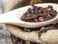 Goździki na ból zęba, naturalny środek łagodzący. Suszone pączki goździkowca na drewnianej łyżce, obok worka z juty.
