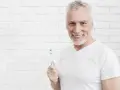Uśmiechnięty starszy pan z siwą brodą trzymający szczoteczkę do zębów. Pokazuje, jak wzmocnić zęby.
