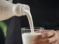 Kefir, naturalny probiotyk, pomaga zwalczać grzybicę jamy ustnej. Biały napój leje się z butelki do szklanki.