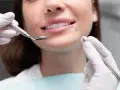 Uśmiechnięta kobieta podczas zabiegu remineralizacji szkliwa. Dentysta używa lusterka i sondy.