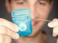 Mężczyzna trzyma niebieskie pudełko z białą nicią dentystyczną. To świetna alternatywa, co zamiast nici dentystycznej, gdy potrzebujesz czystości.