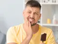 Mężczyzna z bólem zęba, trzymający loda. Jego grymas sugeruje nadwrażliwość zębów na zimno.