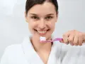 Uśmiechnięta kobieta w szlafroku trzymająca szczoteczkę z pastą. Zastanawia się, czy płukać zęby po myciu, by uzyskać idealny uśmiech.