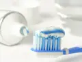 Szczoteczka z biało-niebieską pastą do zębów, zawierającą **sodium fluoride**, gotowa do porannej higieny.