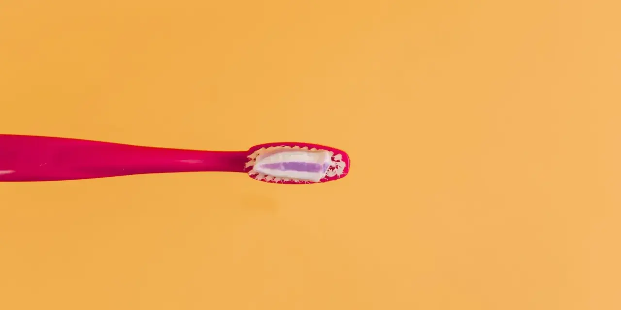 Różowa szczoteczka z pastą, która zawiera fluor. Czy fluor jest szkodliwy? Dyskusja trwa, ale pasta pomaga chronić zęby.
