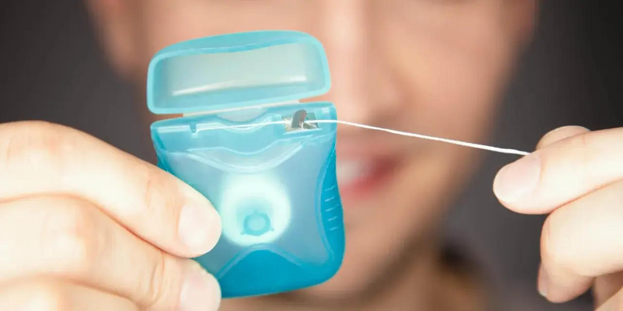 Mężczyzna trzyma niebieskie pudełko z białą nicią dentystyczną. To świetna alternatywa, co zamiast nici dentystycznej, gdy potrzebujesz czystości.