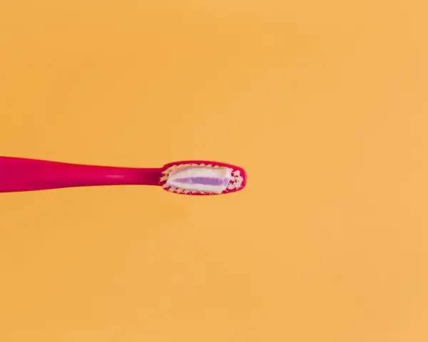 Różowa szczoteczka z pastą, która zawiera fluor. Czy fluor jest szkodliwy? Dyskusja trwa, ale pasta pomaga chronić zęby.