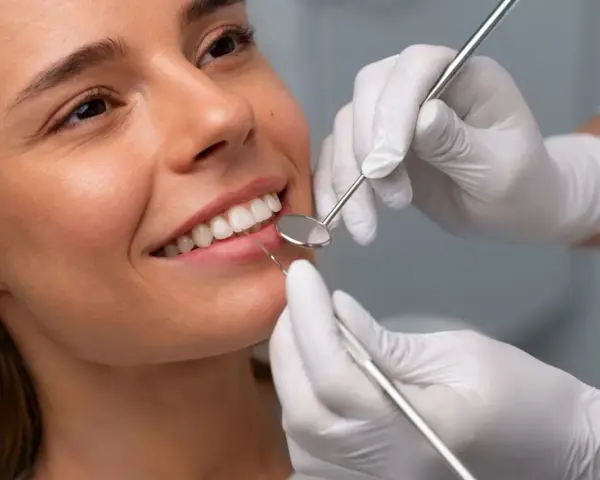Uśmiechnięta kobieta podczas badania stomatologicznego. Dentysta sprawdza zęby, by upewnić się, że bonding nie niszczy zębów.