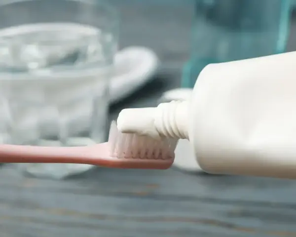 Pasta do zębów na szczoteczce, w tle szklanka wody. Używanie przeterminowanej pasty do zębów może mieć nieprzyjemne skutki.