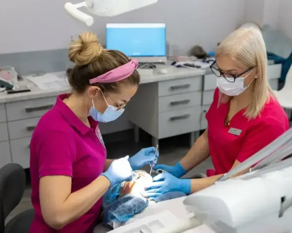 Dwie dentystki w różowych uniformach pracują przy pacjencie. Zastanawiasz się, po jakim czasie działa lekarstwo w zębie?