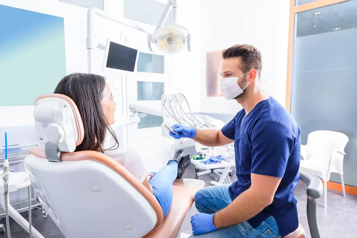 Dentysta w masce rozmawia z pacjentką o problemach z wypadającymi zębami.