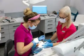 Dwie dentystki w różowych uniformach pracują przy pacjencie. Zastanawiasz się, po jakim czasie działa lekarstwo w zębie?